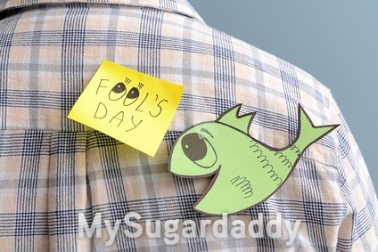 Sticky note with text APRIL FOOLS' DAY and paper fish on back of young man, closeup