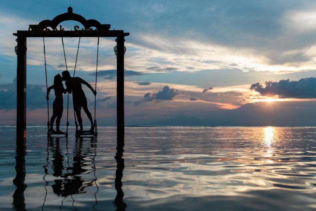 couple kissing on swing on lake at sunset