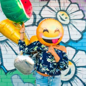 girl holding laughing emoji balloon on april fools' day