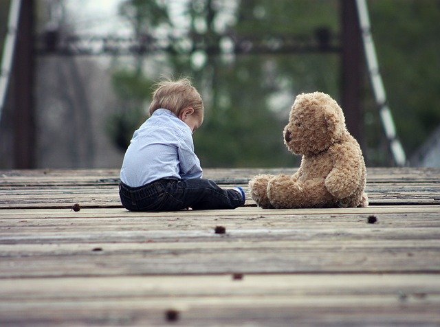 boy sitting head down in front of teddy bear