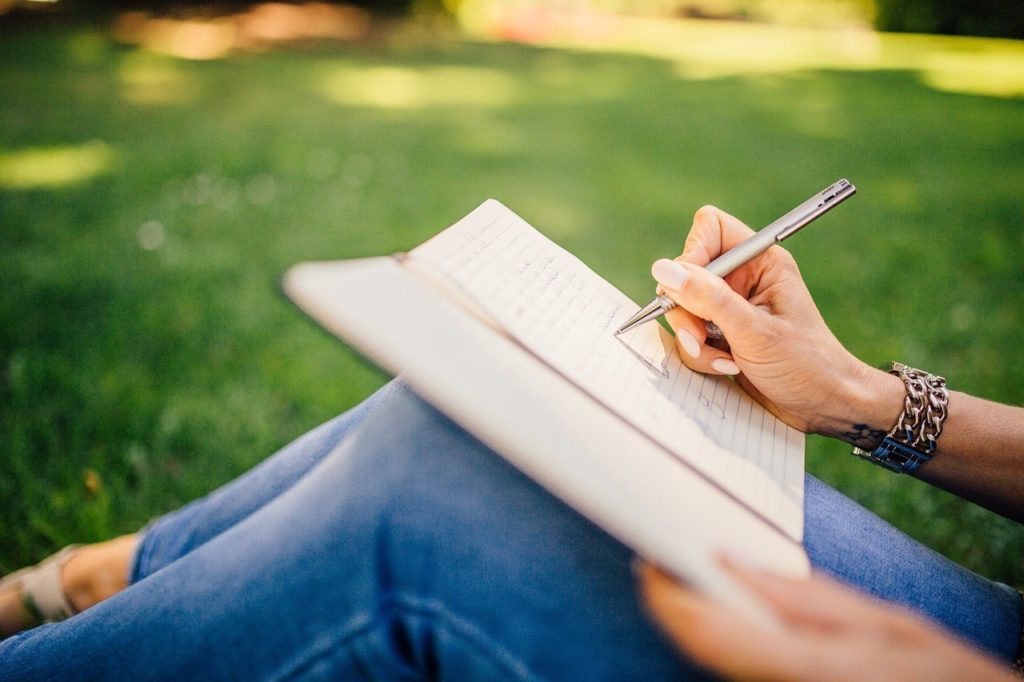 woman writing in her journal by hand on lawn