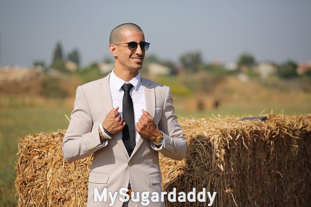 modern gentleman wearing a light grey suit, black tie and sunglasses on field